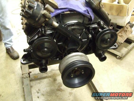 Black engine block with multiple pulleys and a distributor cap, mounted on an engine stand