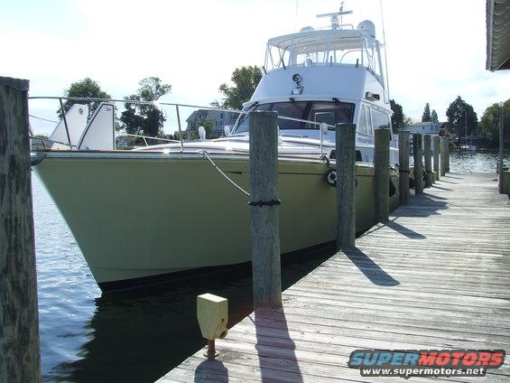 Yacht docked at a wooden pier, light green hull, white superstructure, clear sky
