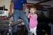 1976 Ford Bronco - A young girl holds a microphone in a garage, with a man and vehicle parts visible in the background.