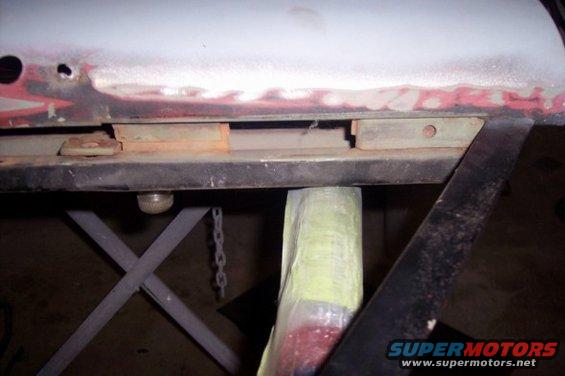 close-up of vehicle frame section with rust and repair work, supported by a jack
