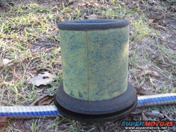 Dirty green and yellow cylindrical air filter with black rubber seals on a grassy ground