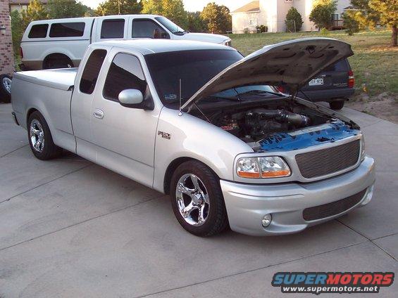 Silver Ford F-150 Lightning pickup truck with hood open, chrome wheels, and tonneau cover