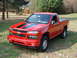 2008 Chevrolet Colorado - A red 2008 Chevrolet Colorado pickup truck with black racing stripes on the hood is parked on a grassy lawn.