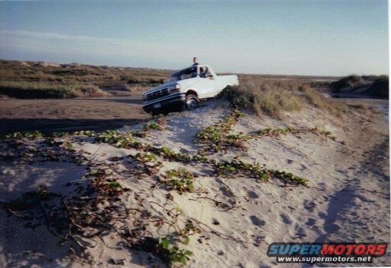 1992 Ford Bronco driving up a sandy dune near the coast