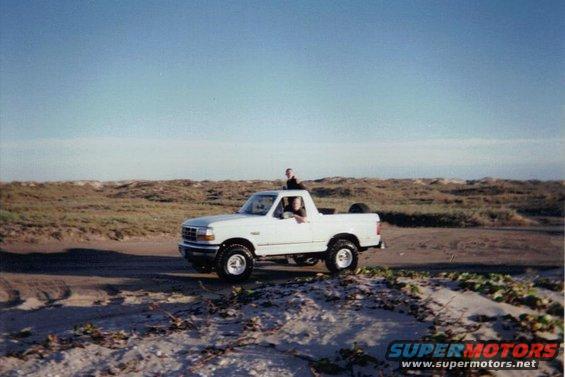 White 1992 Ford Bronco on a sandy road near dunes