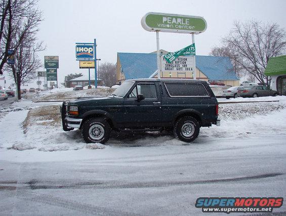 1993 Ford Bronco parked on a snowy street, side view. IHOP and Pearle Vision Center signs visible