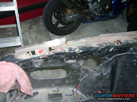 Damaged vehicle frame with red cloth and motorcycle wheel in background