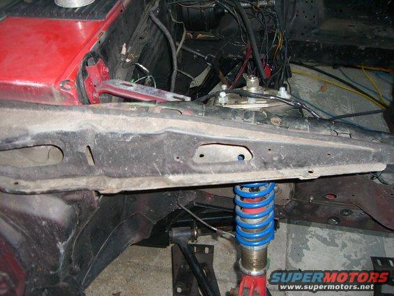 Close-up of car's engine bay showing suspension components and wiring. SuperMotors.net logo visible