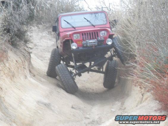 Red Jeep Wrangler off-roading on a dirt path, front view, lifted suspension, winch on bumper