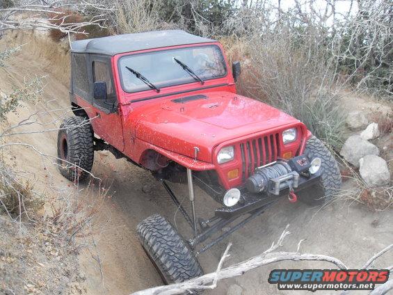 Red Jeep Wrangler with a winch on a steep dirt trail, front passenger side tire is lifted