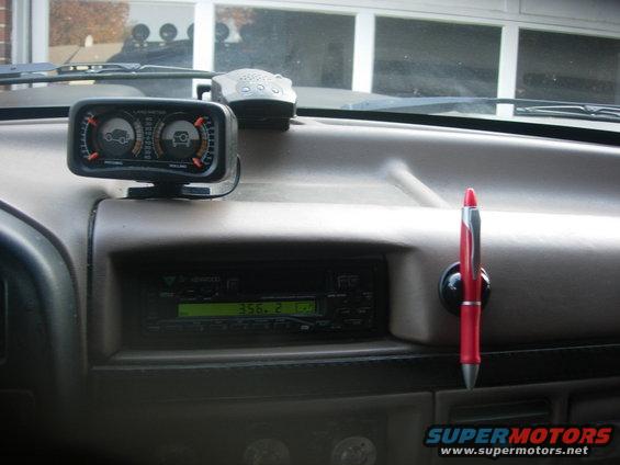 Vehicle dashboard showing a gauge, radio display, and a red pen holder