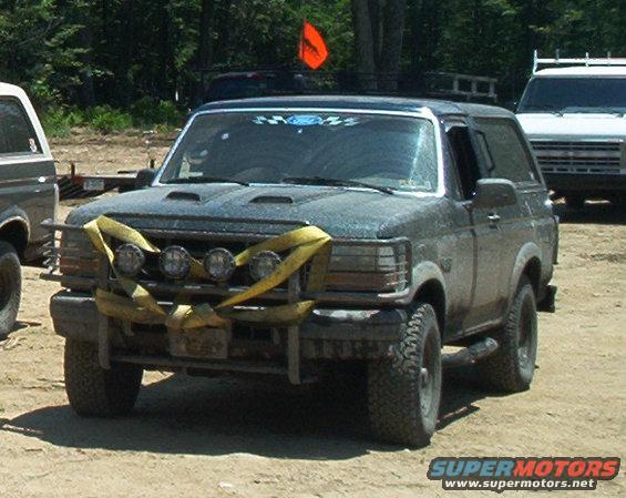 Dark gray Ford Bronco with a yellow tow strap across the front bumper and four auxiliary lights