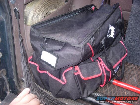 Two black tool bags with red trim and a rolled strap are in the interior of a vehicle