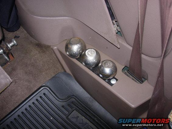 Interior shot of a vehicle's center console area showing three metal balls in a storage compartment. A seatbelt is visible