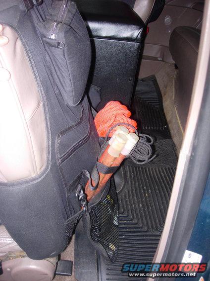 Vehicle interior showing a seat organizer with orange rope and cylindrical objects, and a black floor mat