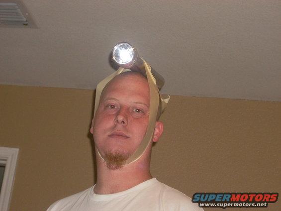 Man wearing a flashlight taped to his head with beige straps