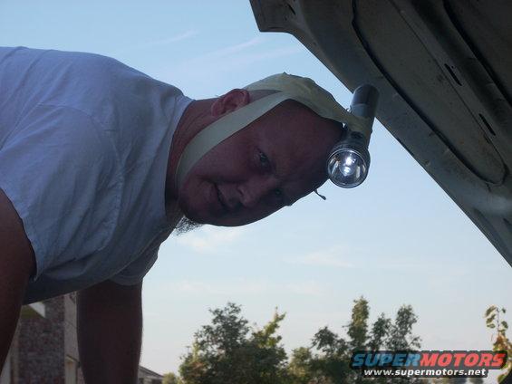 Man with flashlight taped to head works under car hood