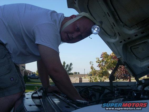 Man with headlamp working on car engine under open hood