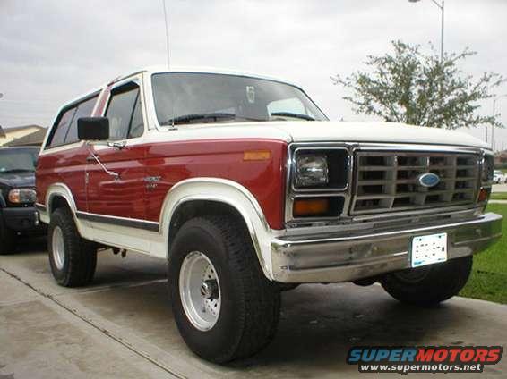 Red and white Ford Bronco, 3/4 front view. Another dark SUV is parked to the left