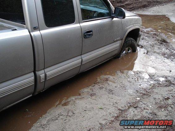 Silver pickup truck stuck in a muddy puddle, front wheel submerged