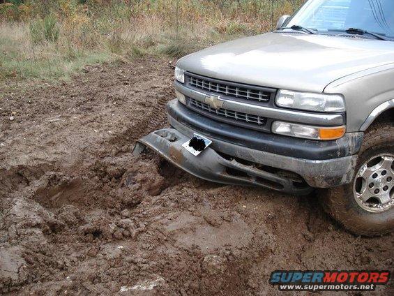 Silver Chevrolet pickup truck stuck in mud, front bumper damaged