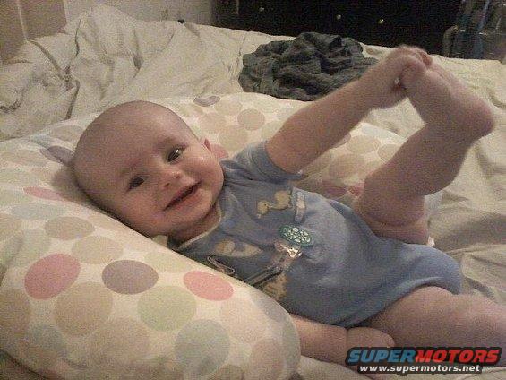 Baby lying on a bed, smiling and holding its foot
