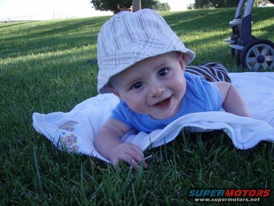 Baby wearing a bucket hat lies on a white blanket on grass