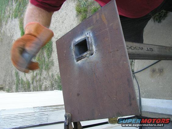 Rusty metal plate with a welded square opening, held by clamps