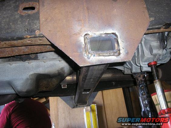 Underbody view of custom metal fabrication on a vehicle frame, supported by a jack