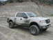 2005 Ford F-150 - A white Ford F-150 pickup truck is heavily covered in mud after driving off-road.