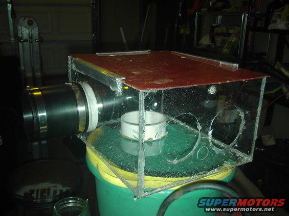 Homemade dust collector made from a clear box with a large black pipe attached to the side, sitting on a green bucket