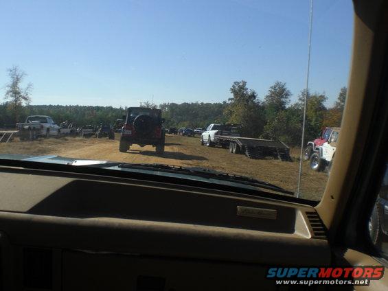 View from inside a vehicle looking out at a field with several off-road vehicles and trailers