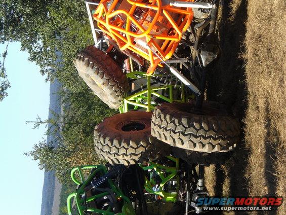 Off-road buggy with orange roll cage and large tires, partially obscured by trees and grass