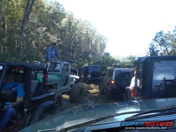 Muddy trail with multiple off-road vehicles, one with a person sitting on top