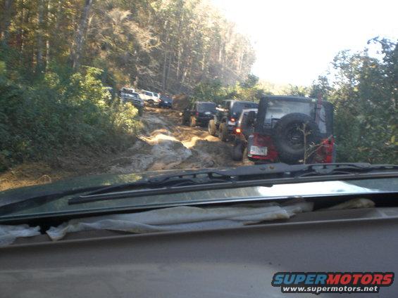 Multiple Jeeps and other off-road vehicles navigating a difficult, muddy trail through a forest