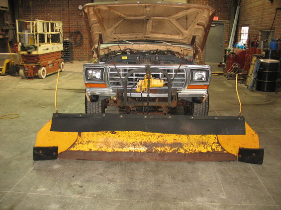 Tan 1979 Ford F-Series truck front view with hood open and a yellow snow plow attached