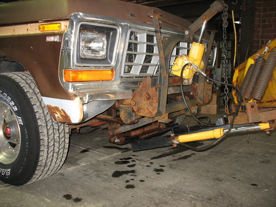1978 Ford F-250 front end with a snow plow attached, showing rust and hydraulic lines