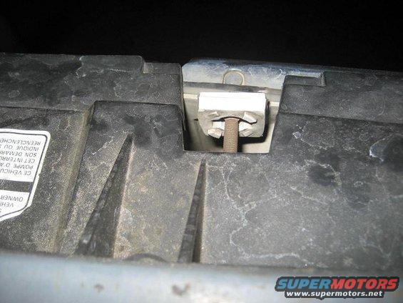 Close-up of a white plastic clip and bolt on a dark plastic radiator support. Some text is visible on a sticker