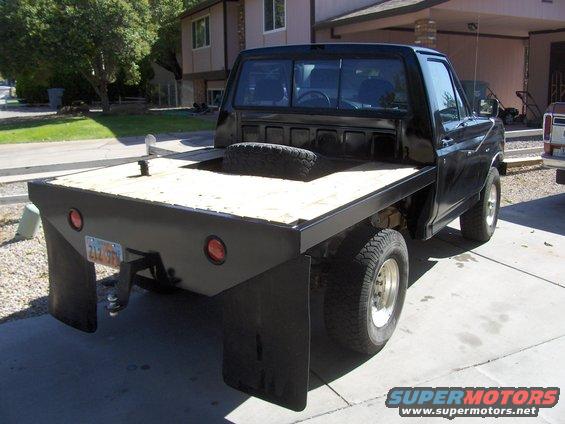 Black flatbed truck with a wooden bed, dual rear wheels, and a spare tire visible