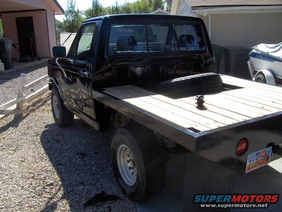 Black flatbed truck with wooden bed, spare tire visible