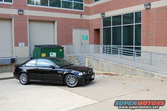 Black 2002 BMW M3 parked next to a brick building with a dumpster