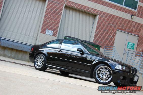 Black 2002 BMW M3 parked by a brick building with large garage doors