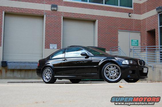 Black 2002 BMW M3 coupe parked in front of a brick building with large roll-up doors
