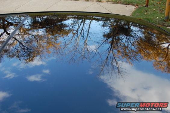 Reflection of autumn trees and blue sky with clouds on a black car roof