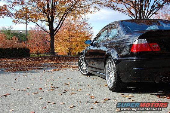Black BMW M3 parked on asphalt with fallen leaves, autumn trees in background
