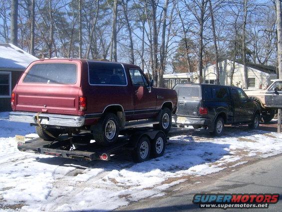 Red SUV on a trailer, with a black pickup truck and another vehicle behind it