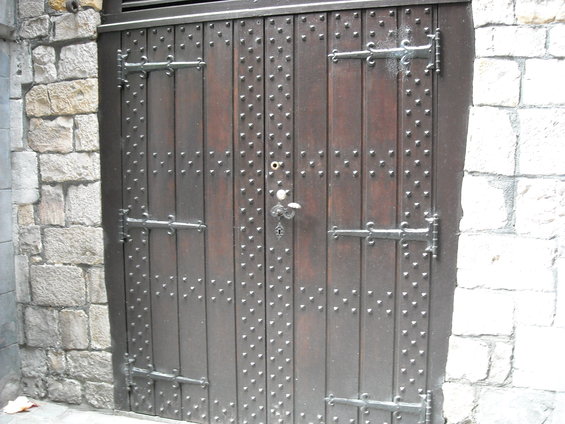 Dark wooden double doors with many metal studs and decorative hinges, set in a stone wall