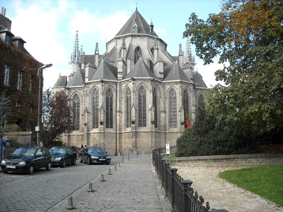 Cars parked on a cobblestone street in front of a large gothic church