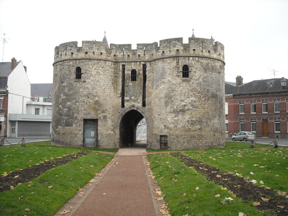 Stone gatehouse with crenellations and arched entryway, a silver car parked nearby