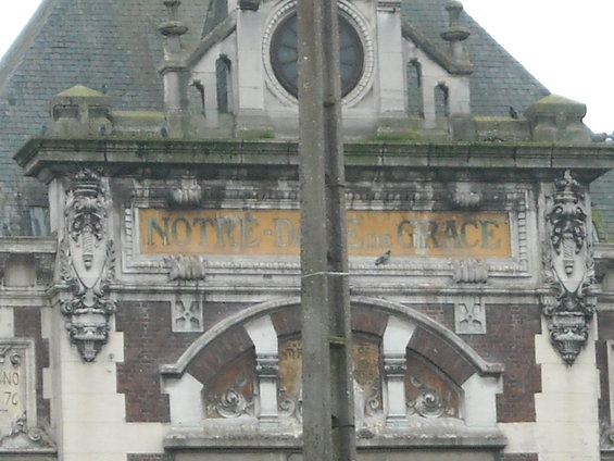 Building facade with text reading 'NOTRE-DAME DE GRACE'. A pigeon is perched on the sign